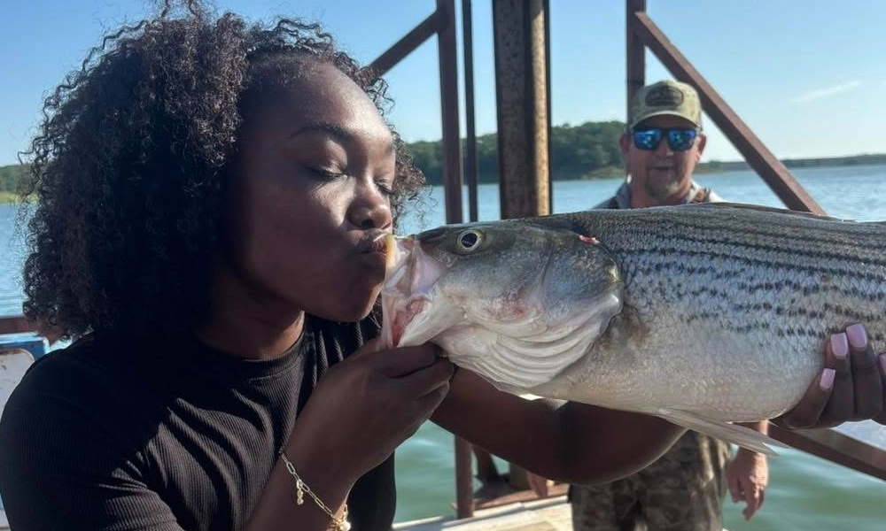 Angler holding a large Lake Texoma striped bass while fishing with a professional guide on a summer fishing trip.